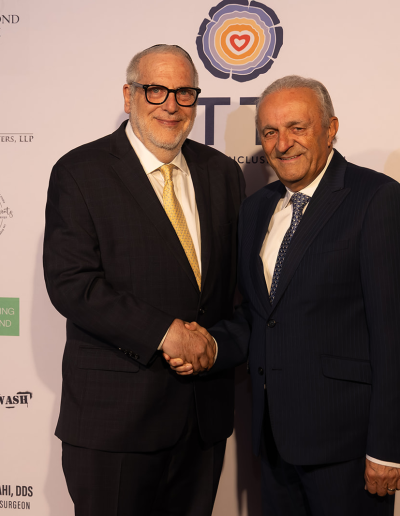 2 men posing together shaking hands in front of the event backdrop.