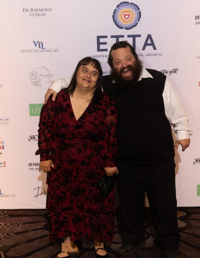 A woman and a man posing together in front of the event backdrop.