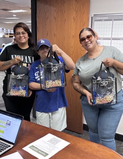 three people holding dodgers goodie bags at etta office