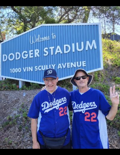 two men in dodgers jerseys in front of welcome to dodgers stadium sign