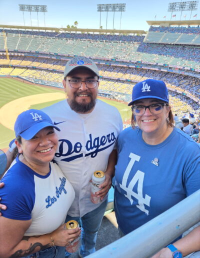 two women and a man wearing dodgers apparel in front of baseball diamond
